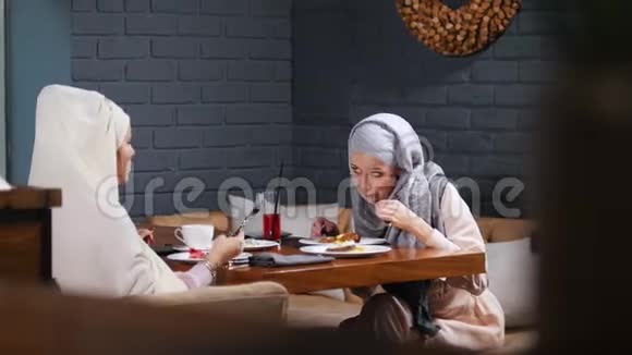 一个穆斯林女人坐在咖啡馆里吃着他们的菜说话视频的预览图