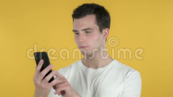 青年男子在黄色背景下使用智能手机视频的预览图