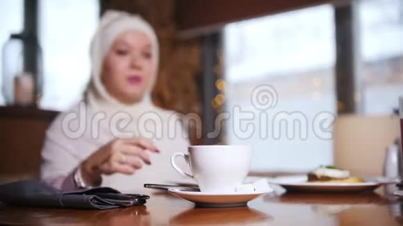 一个年轻的穆斯林女人坐在咖啡馆里喝咖啡视频的预览图