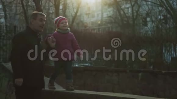 小女孩和她的祖父一起在城市公园沿着女儿墙走着环顾四周微笑着儿童教视频的预览图
