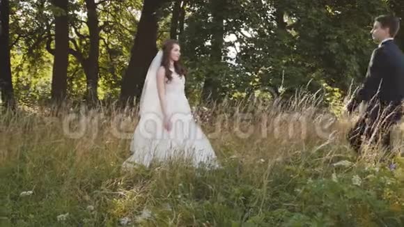可爱的新郎来到新娘面前在阳光明媚的森林里亲吻她视频的预览图