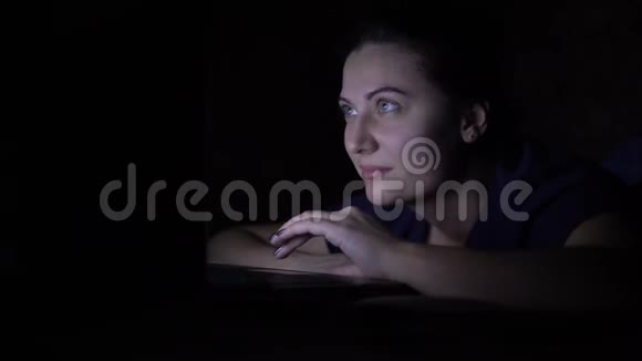 一个女人晚上躺在家里的床上用移动电脑工作孤立光视频的预览图