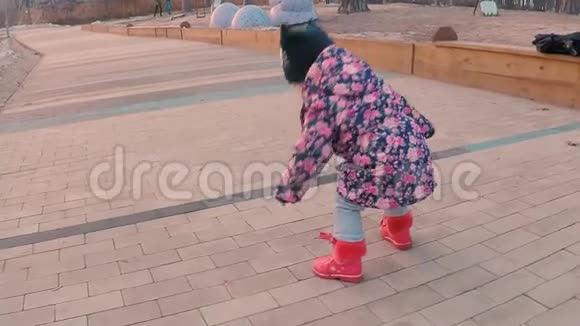 一个穿着五颜六色的粉红色夹克的小女孩在森林郊区的一个公园的操场上叫妈妈视频的预览图