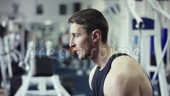 年轻人张开双臂哑铃坐在健身房的长凳上视频的预览图