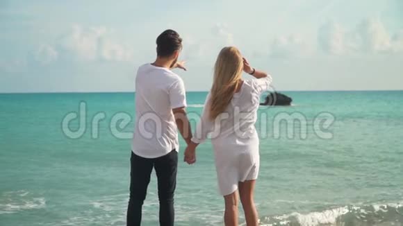 在海滩上牵手美丽的年轻夫妇的后景视频的预览图