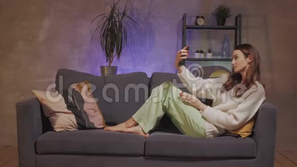 一个年轻的女人坐在舒适的房间里的沙发上自拍并微笑着视频的预览图