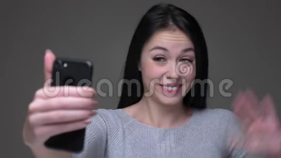 一位年轻漂亮的褐发白种人女性的特写镜头她在电话上打了个视频电话向背景打招呼视频的预览图