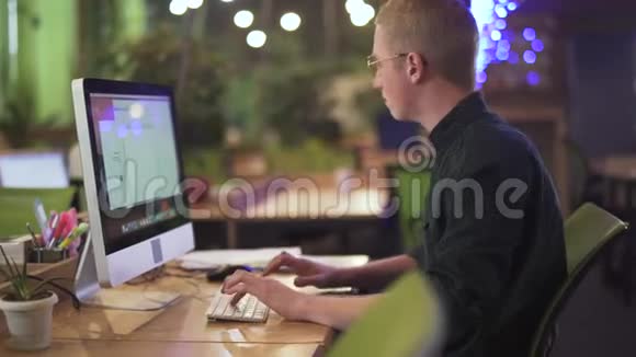戴眼镜的年轻有思想的男人坐在现代电脑前大办公室打字的画像视频的预览图