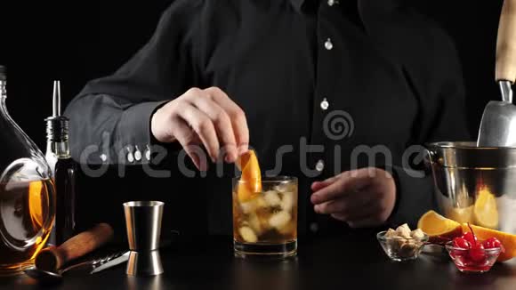 老式鸡尾酒酒保把一片橙色的皮肤放进鸡尾酒里然后他把红樱桃放进成品饮料里视频的预览图