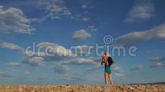 年轻女子穿着绿色比基尼带着一个婴儿在一个荒凉的海滩上背景是蓝天和白云产后视频的预览图