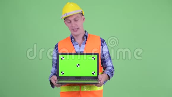 快乐的年轻建筑工人一边说话一边展示笔记本电脑视频的预览图