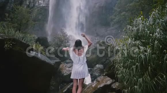 在史诗般的斯里兰卡丛林瀑布中带着张开双臂享受自由时刻的快乐年轻旅游妇女视频的预览图