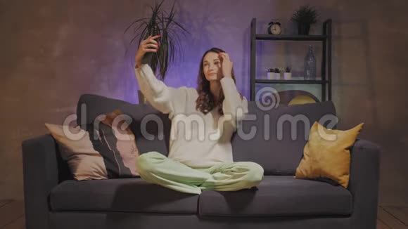 一个年轻的女人坐在舒适的房间里的沙发上自拍并微笑着视频的预览图