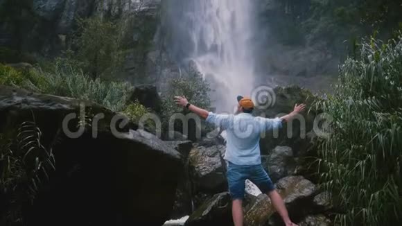 后景兴奋的年轻游客双臂张开享受斯里兰卡丛林瀑布的史诗般的自由时刻视频的预览图