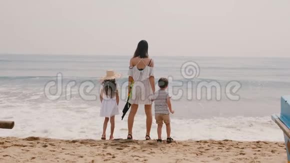 后景快乐的年轻妈妈带着小男孩和小女孩在热带海滨度假时看海浪慢动作视频的预览图