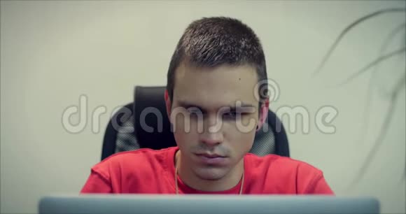 年轻人程序员或商人的肖像坐在办公室里带着一张认真思考的脸用笔记本电脑工作视频的预览图