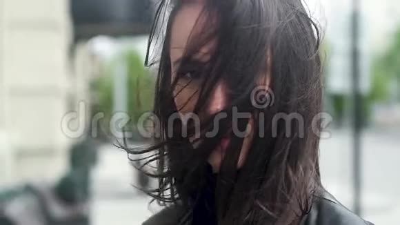 一个年轻迷人的女孩的特写肖像一阵强风用头发遮住了他的脸城市街道的背景视频的预览图