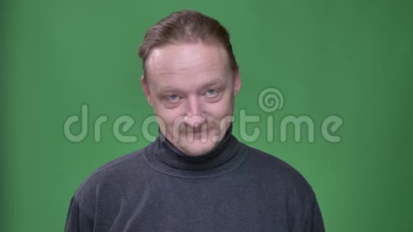 有胡子的中年男子的肖像在绿色的背景上偷偷地微笑着进入镜头视频的预览图