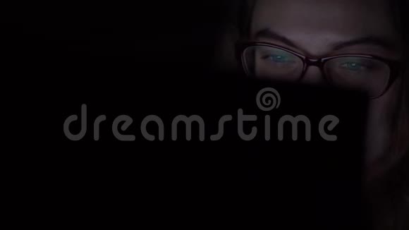 戴眼镜的年轻女孩躺在床上时使用笔记本电脑夜间射击视频的预览图