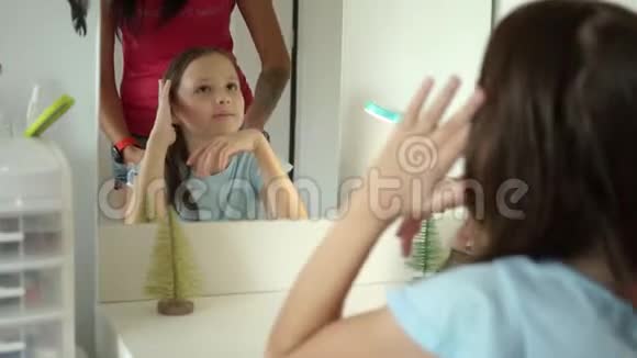 可爱的青春期前的女孩在妈妈梳头的时候到处看镜子视频的预览图