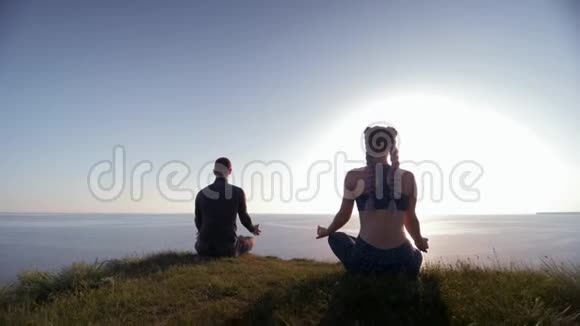 精神世界男人和女人坐在山顶上看着大海在陆地上以莲花的姿势冥想观看视频的预览图
