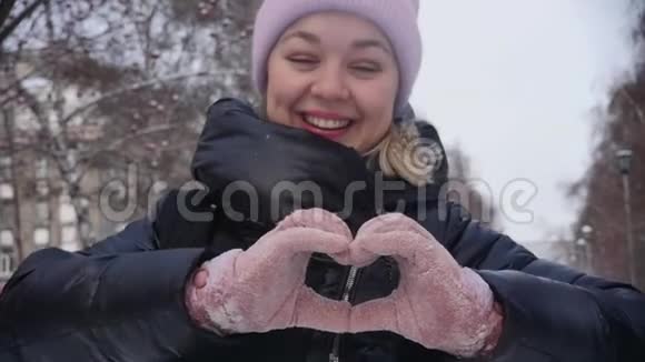 双手在冬天的手套中使心脏的形状成为城市小巷背景上的标志慢动作爱的冬天视频的预览图