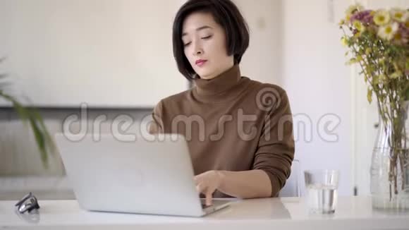 一位亚洲女性留着短发在白色家庭办公室工作手提电脑视频的预览图
