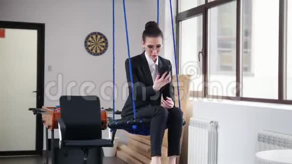 商业概念一个女人坐在办公室的秋千上用她的电话说话视频的预览图