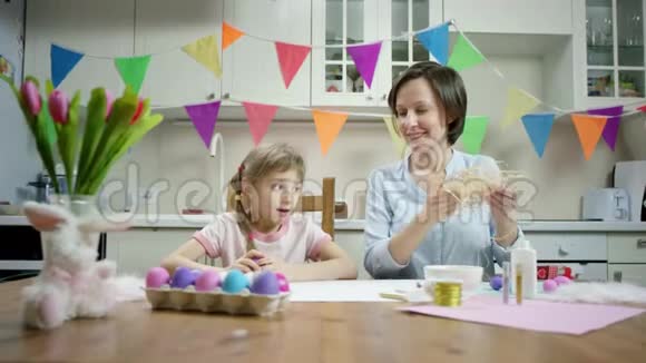 母亲和女儿坐在餐桌前一起用彩色复活节彩蛋制作巢穴然后在厨房里嬉戏视频的预览图