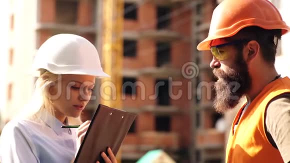 男女工程师控制施工过程建筑区戴头盔的工人工程师和建筑师视频的预览图