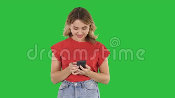 年轻的漂亮女人穿着t恤在绿色屏幕上使用她的智能手机Chroma键视频的预览图