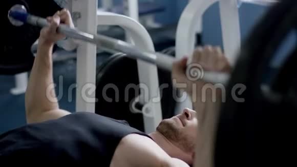 年轻的健美运动员在健身房里举起杠铃躺在一个上视频的预览图