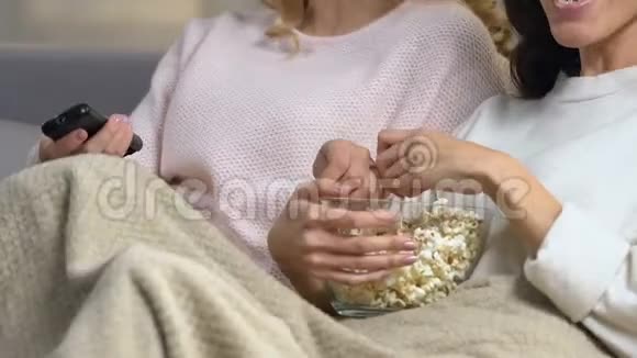 两个漂亮的朋友坐在沙发上吃爆米花笑着看喜剧电影视频的预览图