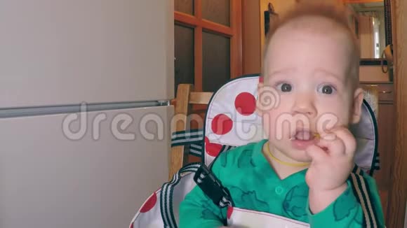 一个小可爱的小男孩长着两颗较低的牙齿坐在厨房的餐椅上吃着稻草笑容满面视频的预览图