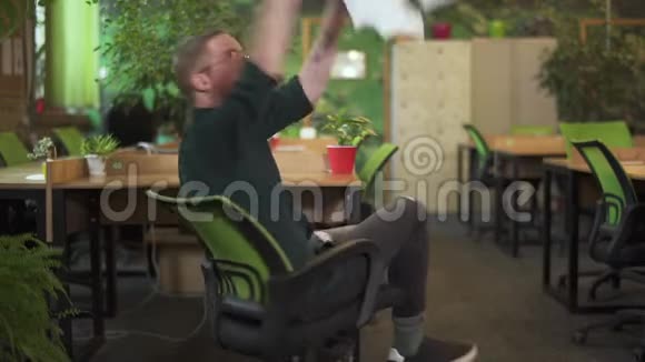 英俊的年轻人在现代绿色环保办公室骑椅子和扔纸严肃的脸慢动作视频的预览图