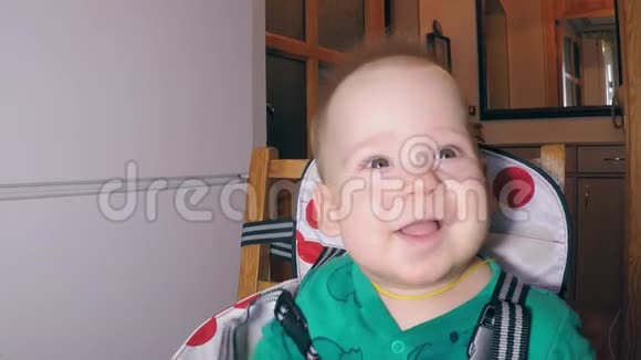 小可爱的小男孩有两个较低的牙齿在厨房里坐在靠近喂食椅上时笑容满面视频的预览图
