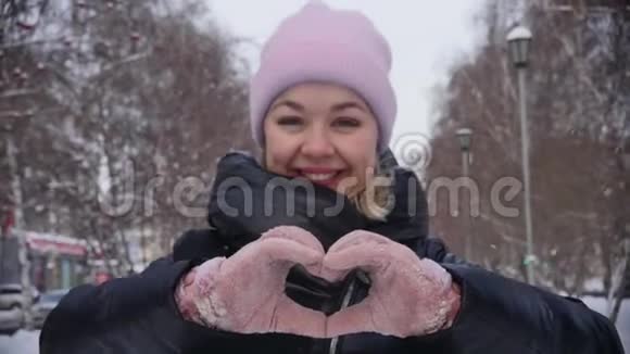 双手在冬天的手套中使心脏的形状成为城市小巷背景上的标志慢动作爱的冬天视频的预览图