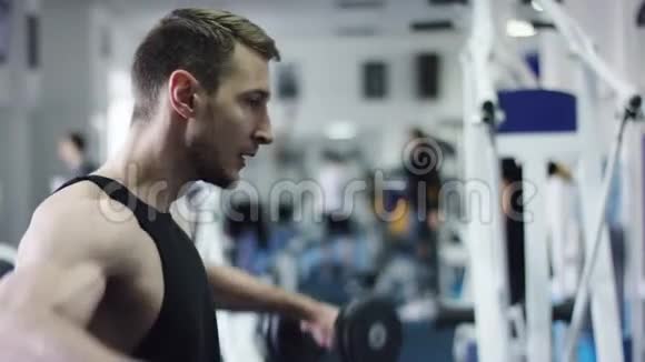 一名年轻的运动员在健身房的长凳上用哑铃伸展双手的侧面照片视频的预览图