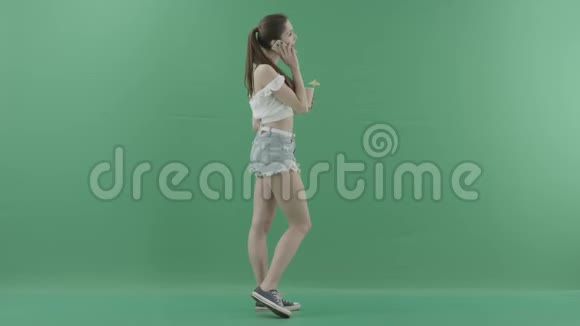 漂亮女人在绿色背景下喝鸡尾酒时打电话视频的预览图
