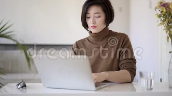一位亚洲女性留着短发在白色家庭办公室工作手提电脑视频的预览图