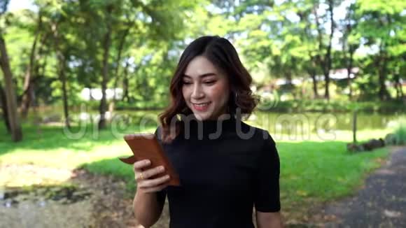 女人在公园里散步和使用智能手机视频的预览图