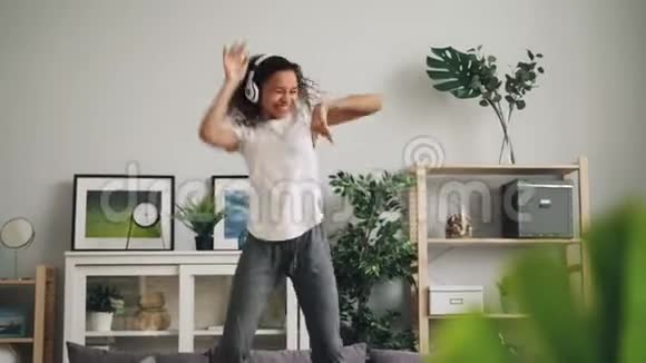 美国一位有音乐感的非洲裔妇女正在家里的沙发上跳着舞带着耳机听音乐享受着节奏视频的预览图