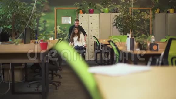 快乐微笑的男人和女人下班后在现代办公室休息年轻人开着漂亮女孩坐在办公椅上视频的预览图