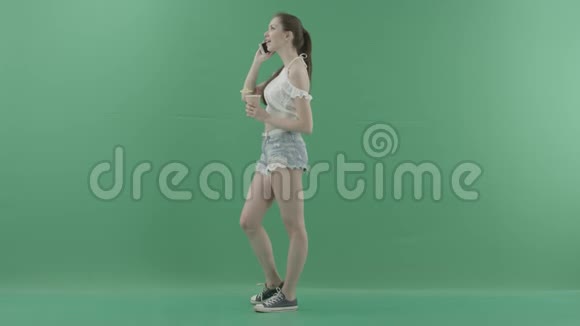 有魅力的年轻女性在绿色背景下喝鸡尾酒时打电话视频的预览图