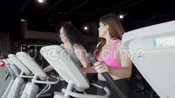 两个以上大小的女人在健身房锻炼时在椭圆教练机上交谈视频的预览图