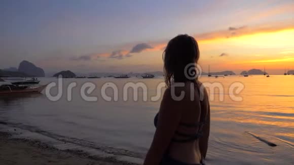 年轻女孩穿着裙子在日落海滩上散步欣赏海景和海岛景色女孩沿着海滩散步享受一个视频的预览图