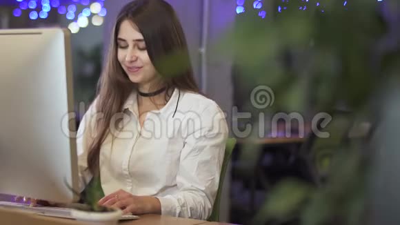 在现代办公室背景下一位年轻漂亮的女士在电脑旁工作或聊天视频的预览图