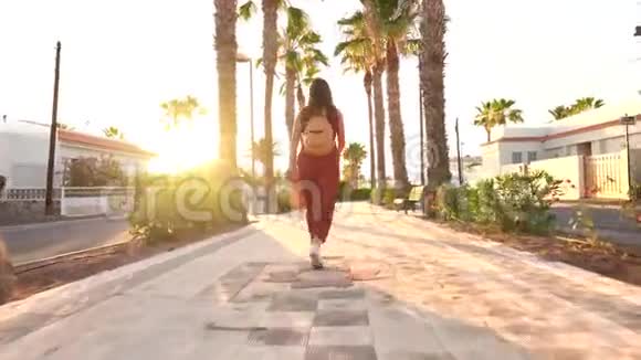 日落时分戴着一顶黄色大帽子的快乐女人沿着棕榈巷奔跑视频的预览图