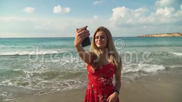 一幅美丽的年轻女子的肖像金发在她的手机上自拍在海滩附近可爱的女孩花时间视频的预览图