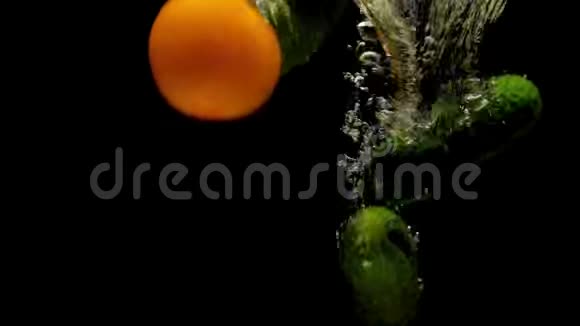 Tomatos和黄瓜在黑色背景的透明水中掉落视频的预览图